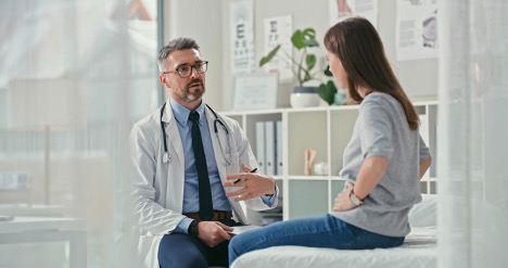 Mature doctor sitting with his patient in the clinic and asking questions during a consultation