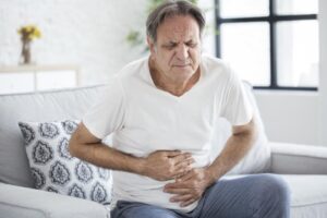 A senior man sitting on the sofa is suffering from severe constipation He is holding his stomach with both hands